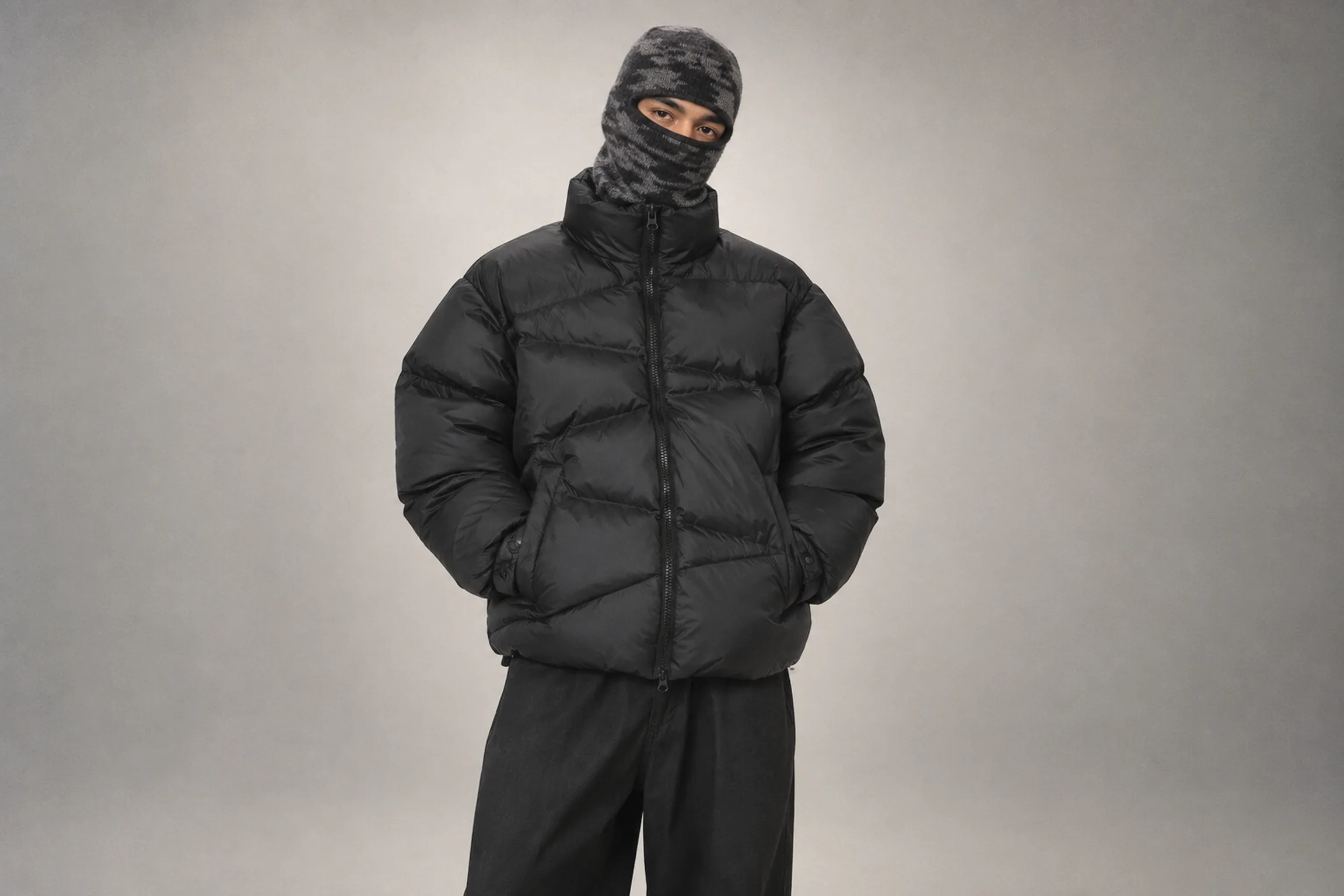 Model in a camo knit balaclava and The Americana Zip Padded Jacket on a grey studio backdrop